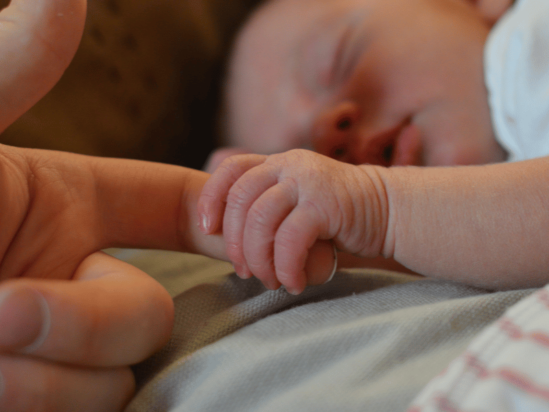 Close-up of a newborn's tiny hand gripping a parent's finger, a powerful image of new life and parental connection.