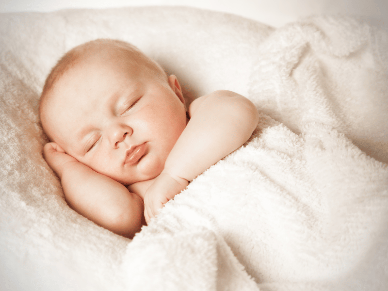 Newborn sleeping peacefully in a soft white blanket, demonstrating the importance of a comfortable sleeping environment for infants.