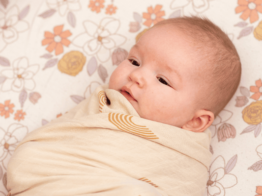 Newborn baby wrapped cozily in a floral patterned swaddle blanket, looking serene.