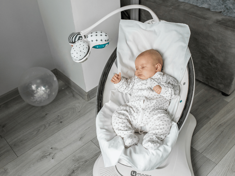 Newborn sleeping peacefully in a modern baby swing with a hanging mobile, in a well-lit nursery