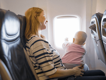 Mother smiling at her baby reaching for airplane window during flight.