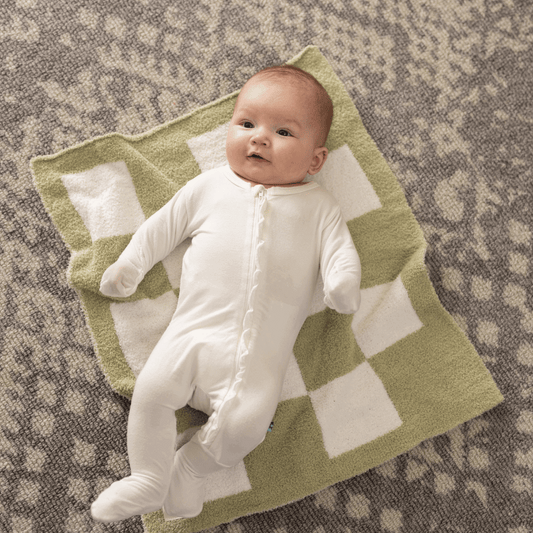 Infant smiling while lying on a Luxe Checkered Mini Baby Blanket in Matcha Green by Stella Moon Co., set against a stylish carpet.