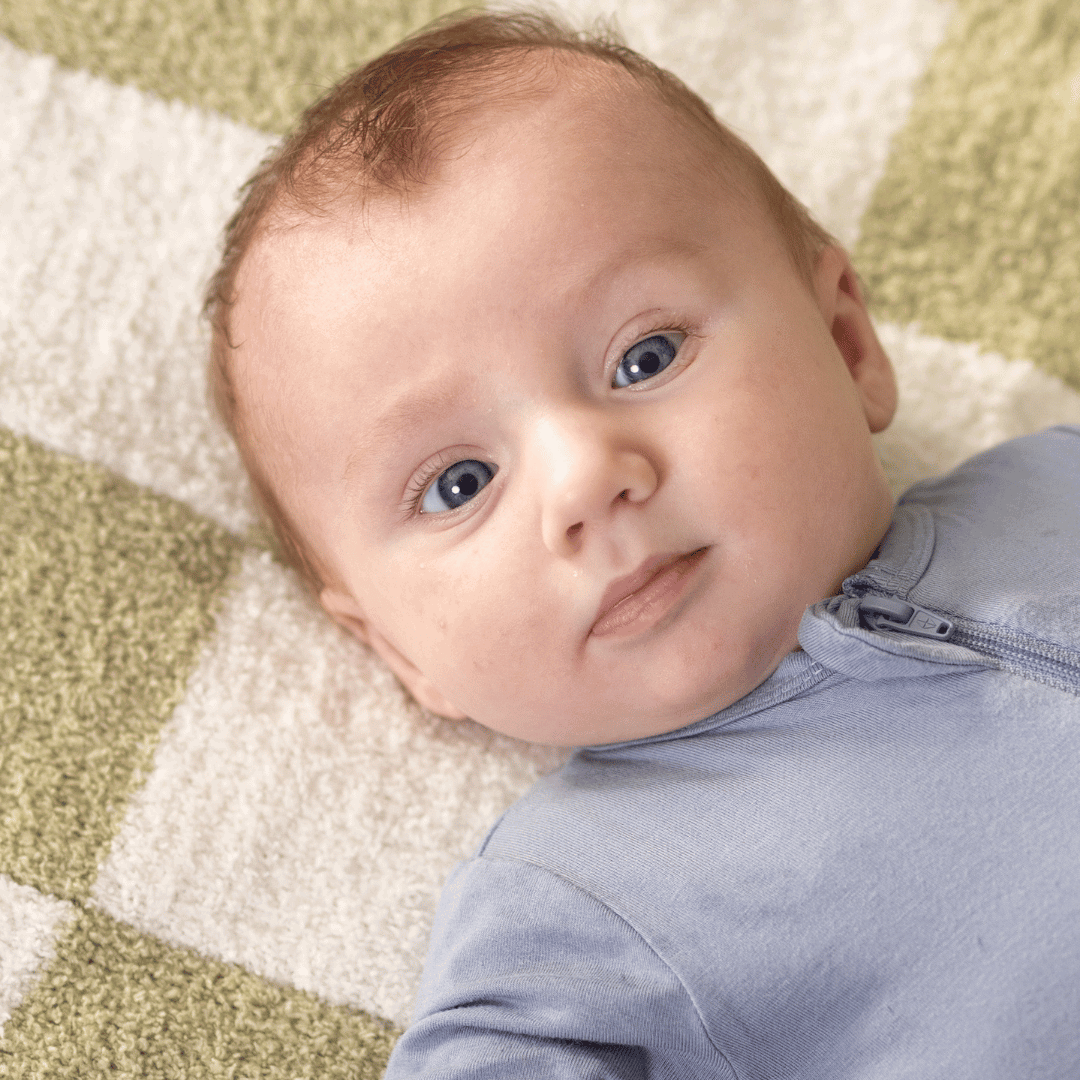 Close-up view of a baby lying on a Luxe Checkered Mini Baby Blanket in Matcha Green, showing a curious expression and bright eyes.