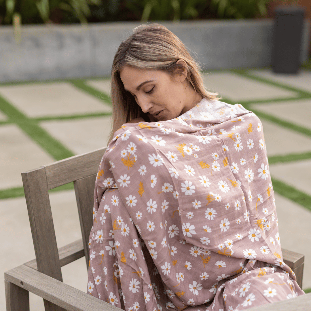 Woman wearing a daisy-print bamboo swaddle as a nursing cover outdoors.