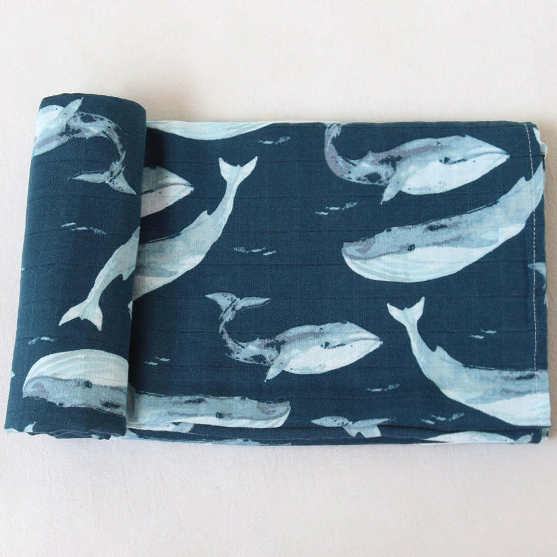 Navy blue bamboo swaddle blanket with a whale pattern, neatly folded on a white background.