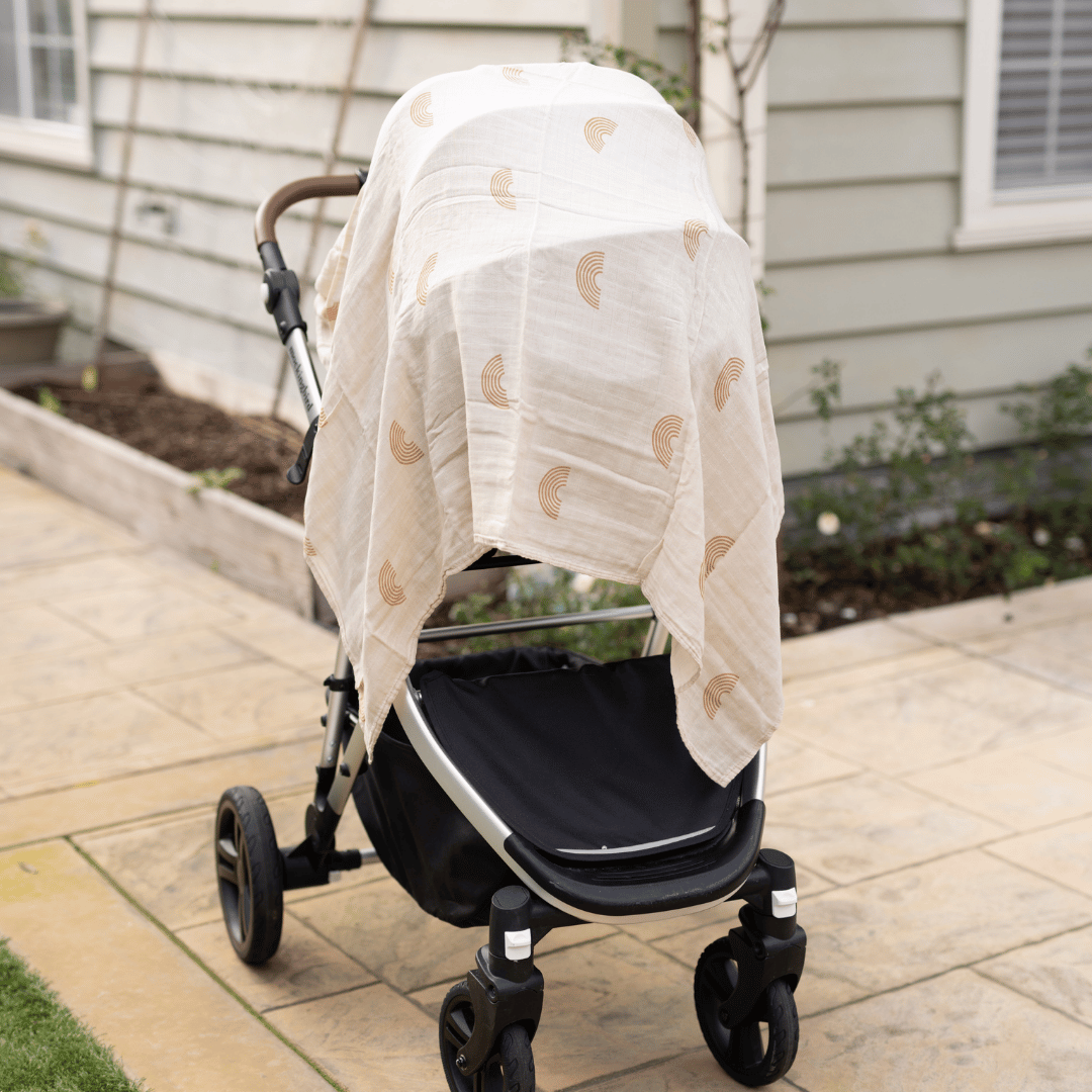 Organic bamboo swaddle blanket with a minimalist rainbow pattern draped over a baby stroller as a breathable car seat cover outdoors.