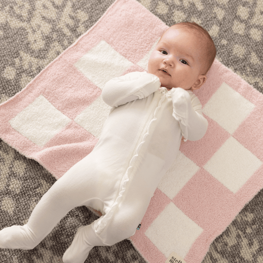 Baby in a white outfit lying on the Pink Luxe Blanket, featuring a soft pink and white checkered design for a cozy and charming look.