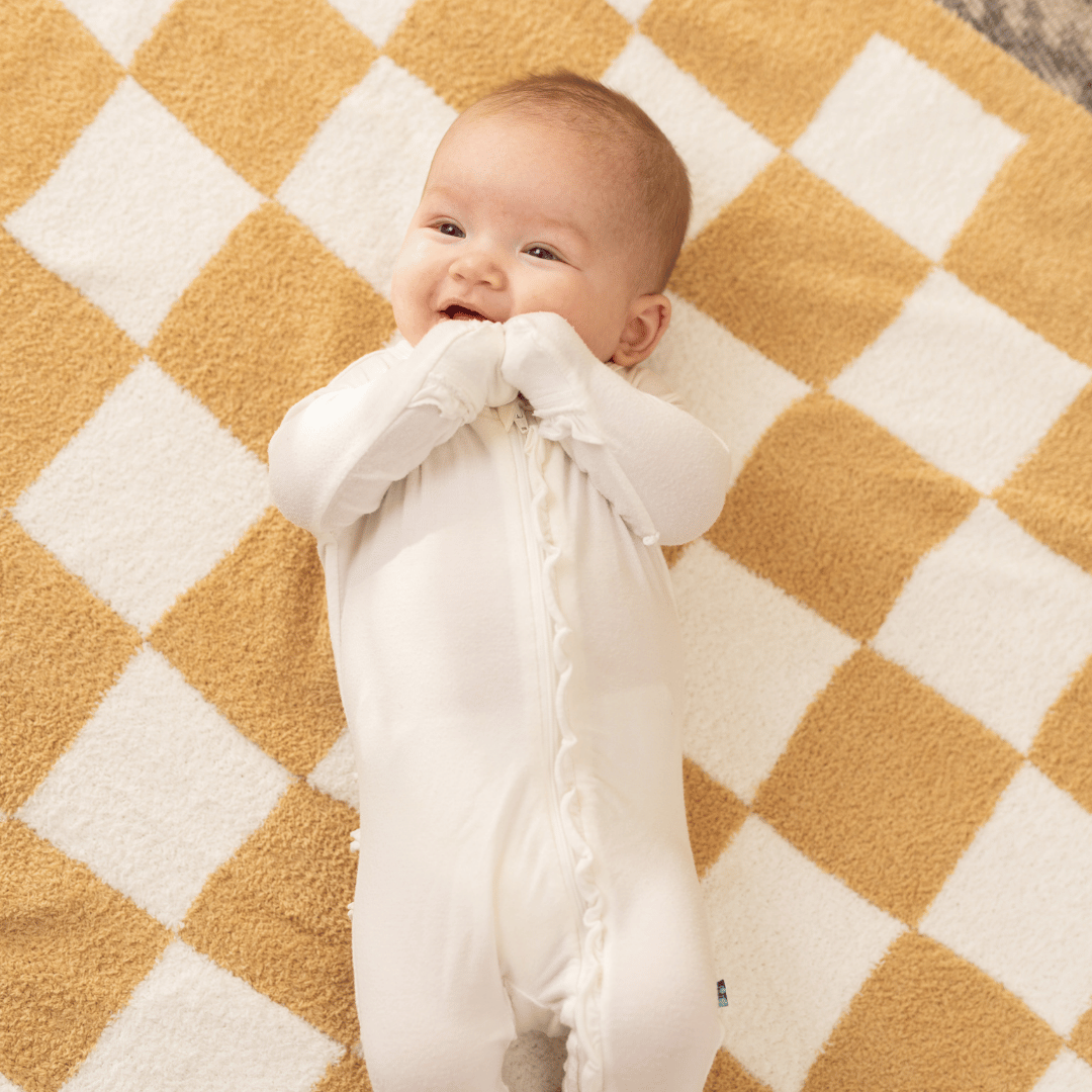 Adorable baby smiling while lying on a checkered blanket, capturing the cozy comfort and cheerful moments of early childhood.