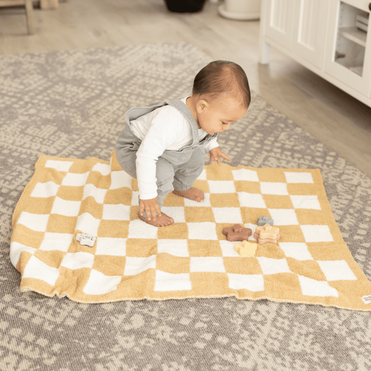 Baby playing on the Luxe Checkered Baby Blanket in Sand, highlighting its plush texture and versatile use as a play mat or nap-time essential.