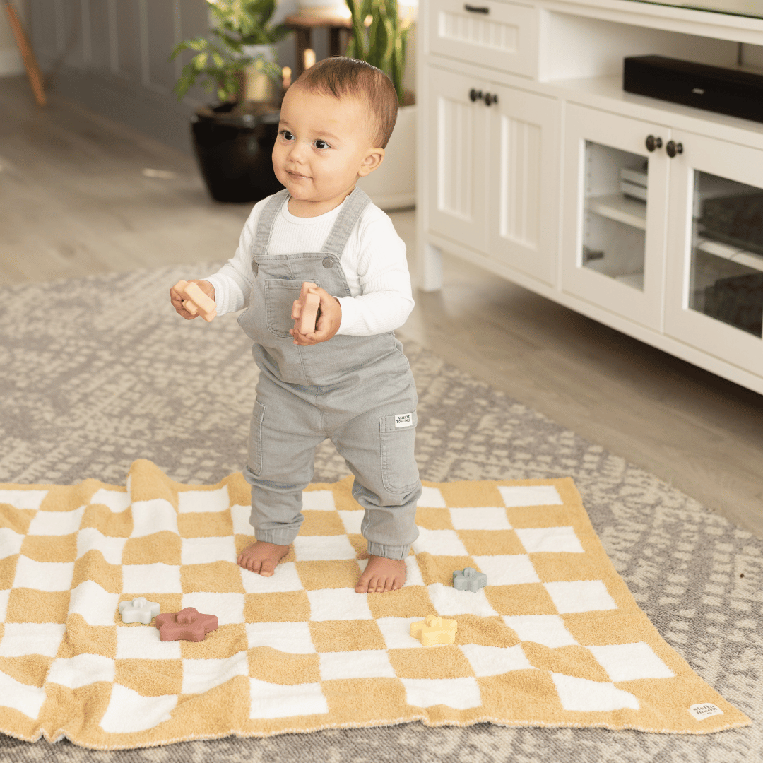 A joyful toddler taking first steps on a StellaMoon's checkered blanket, surrounded by toys and the warmth of home, highlighting a milestone moment.