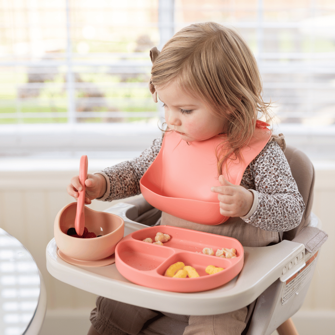  Toddler girl eating berries from a pink silicone bowl at a high chair, enhancing mealtime ease.