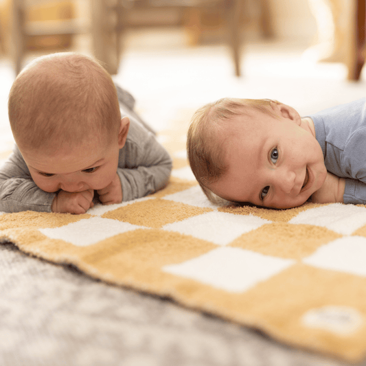 Twin babies enjoying tummy time on a StellaMoon checkered blanket, capturing a delightful moment of early exploration and bonding.