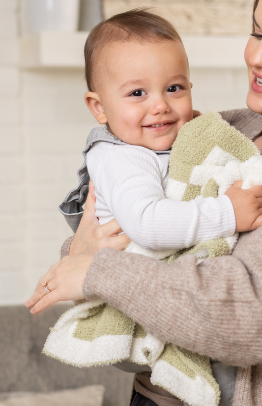 Adorable baby holding and cuddling StellaMoon's Luxe Checkered Baby Blanket in Matcha, showcasing its plush texture and comforting checkered design.