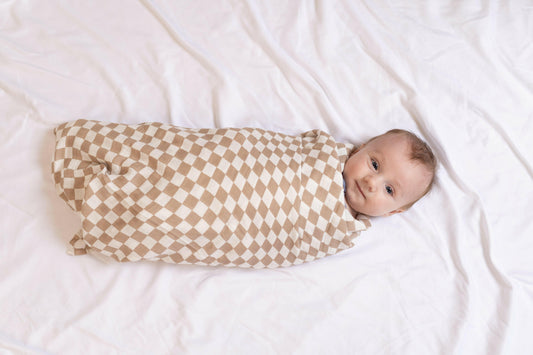 A serene baby swaddled snugly in StellaMoon's Checkered Bamboo Swaddle. The timeless checkered pattern contrasts beautifully with the soft innocence of the baby, showcasing the comfort and breathability of the bamboo-cotton blend fabric. A perfect emblem of warmth and care.