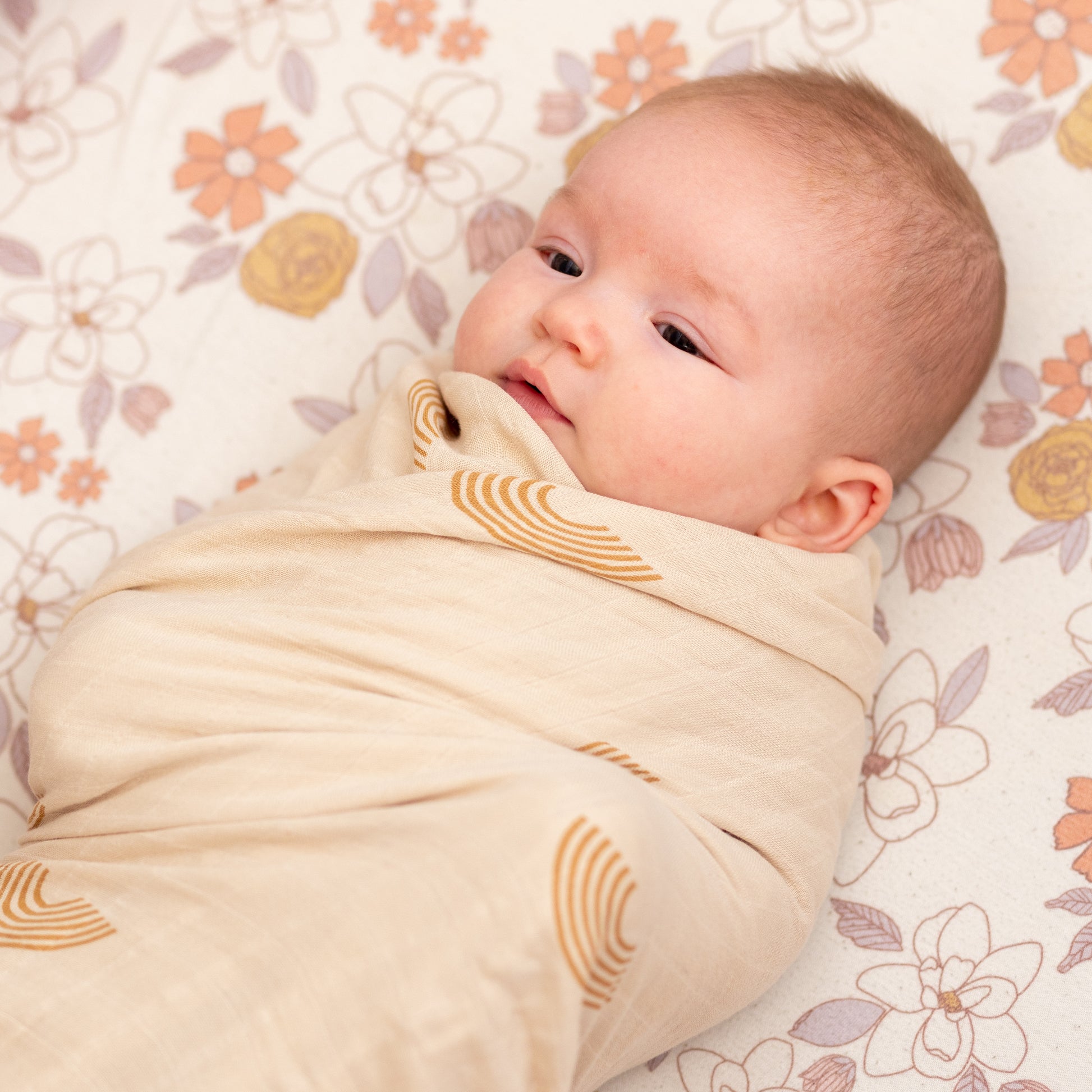 A joyful baby snuggled up in StellaMoon's Multi-use Bamboo Swaddle, showcasing a vibrant rainbow pattern. The premium bamboo-cotton blend ensures a soft touch against the baby's skin. The lively rainbow design lights up the room, reflecting hope, love, and the magic of childhood moments.