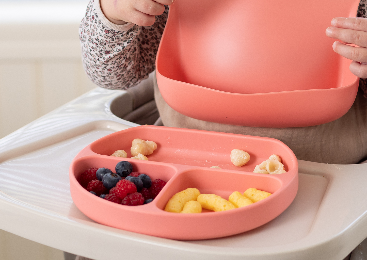 Baby using the StellaMoon Silicone Suction Plate in Sherbert during mealtime, with a matching StellaMoon bib draped around their neck, showcasing a coordinated and spill-proof dining experience.